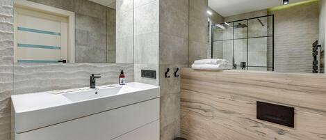 Une salle de bain moderne avec un grand miroir, un lavabo et un espace douche.