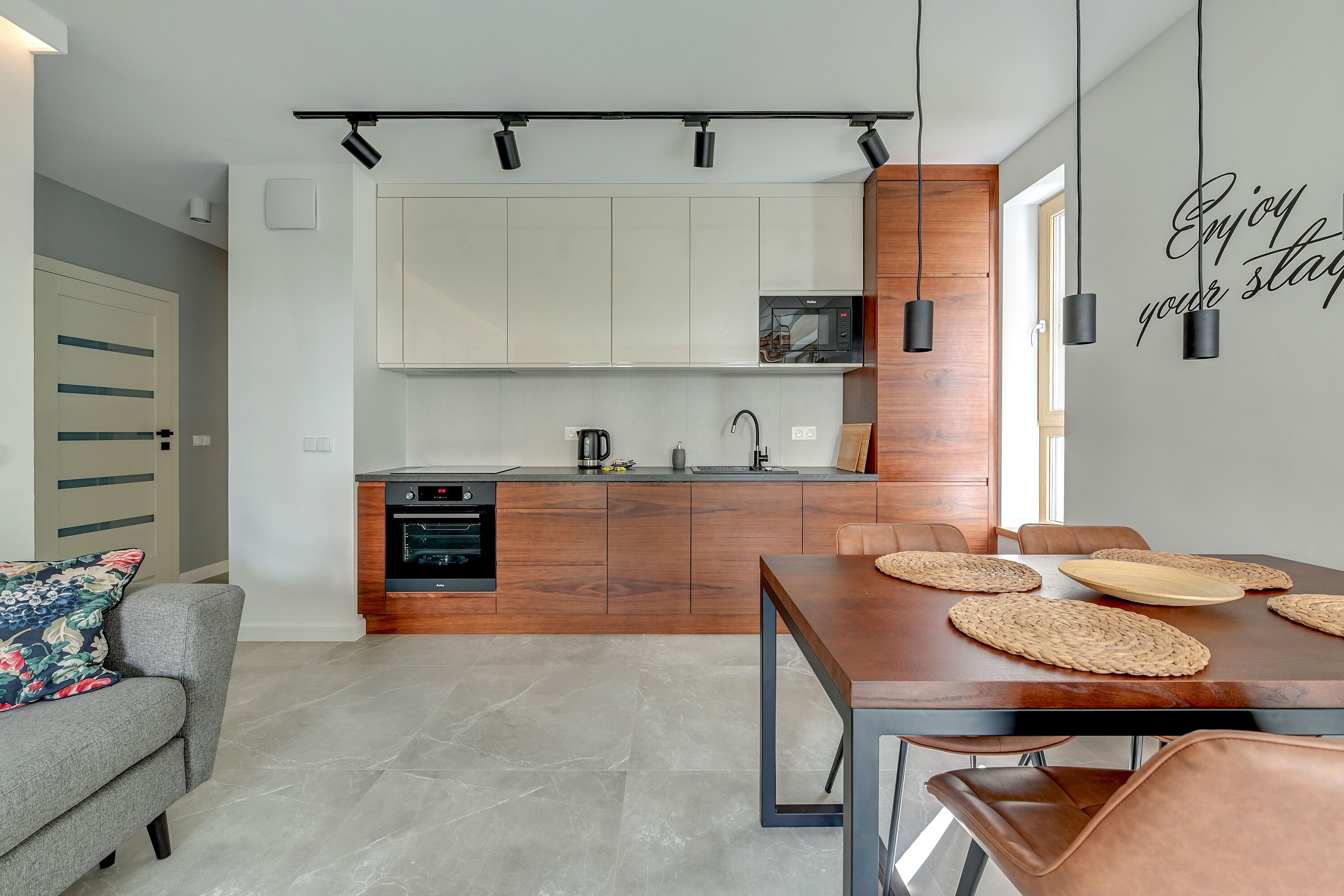 A modern kitchen with wooden cabinets, a built-in microwave, and a dining area with a table and chairs.