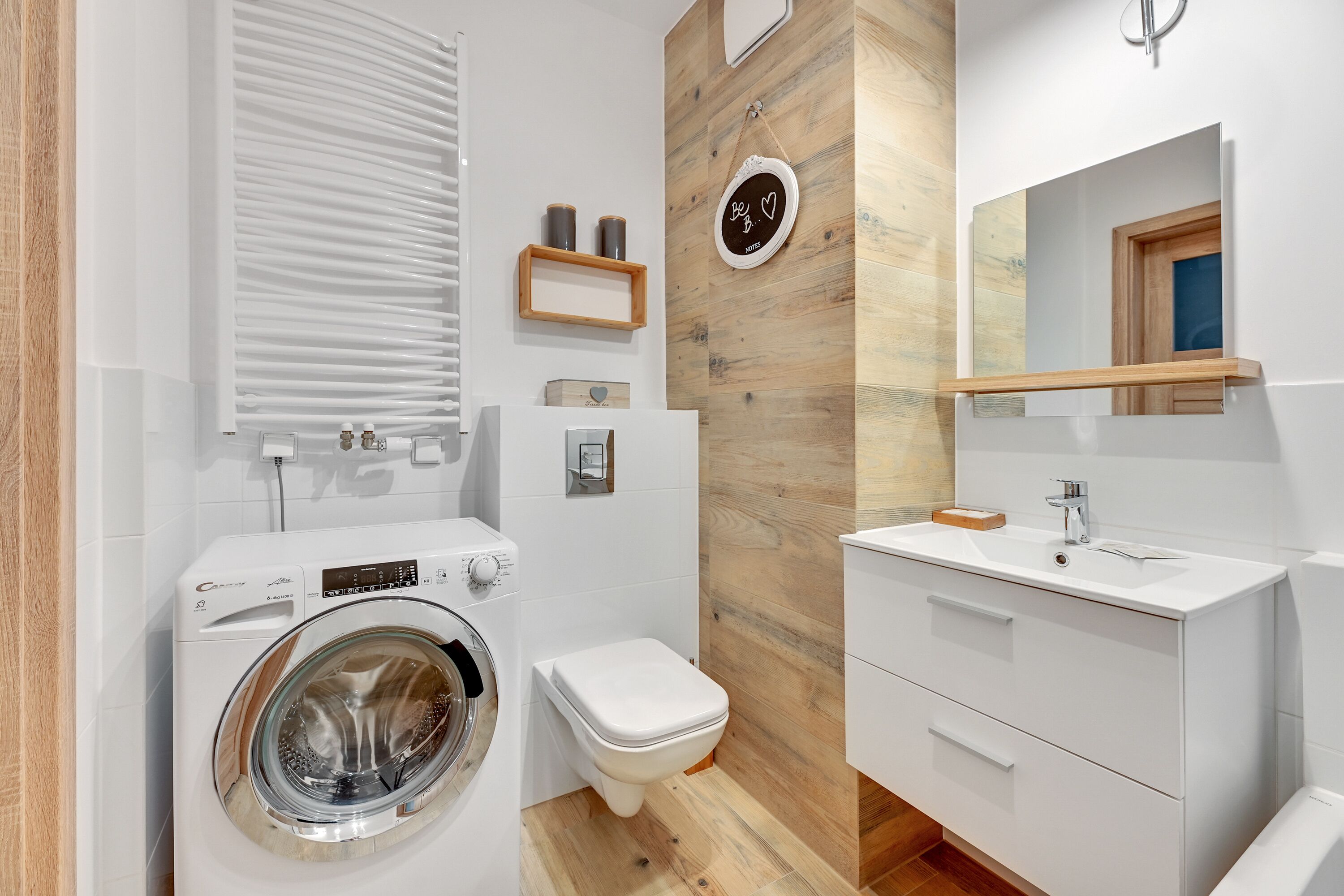 A modern bathroom with a washing machine, toilet, and vanity with a mirror.