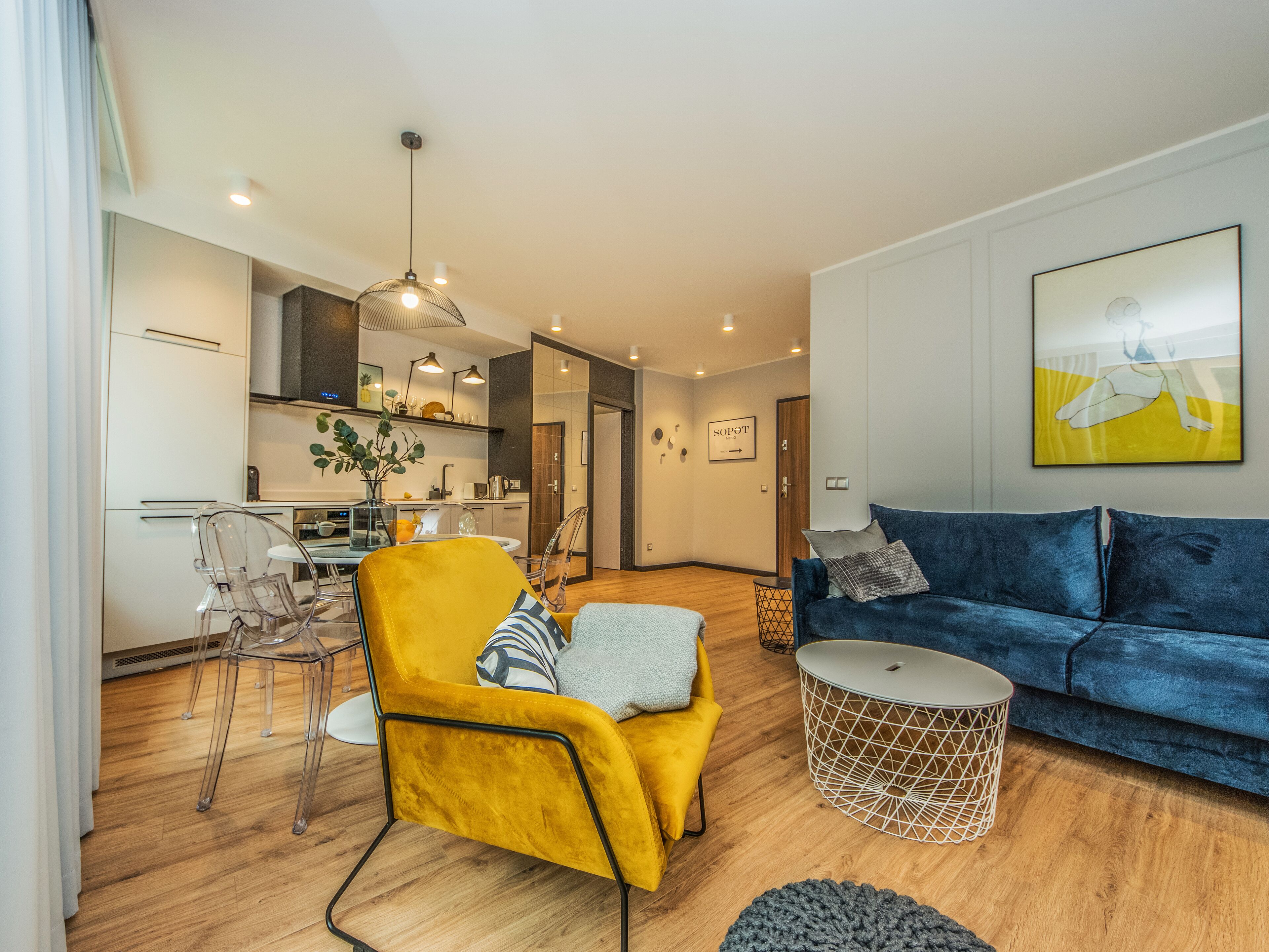 Una sala de estar moderna con un sillón amarillo, un sofá azul y una mesa de vidrio transparente.