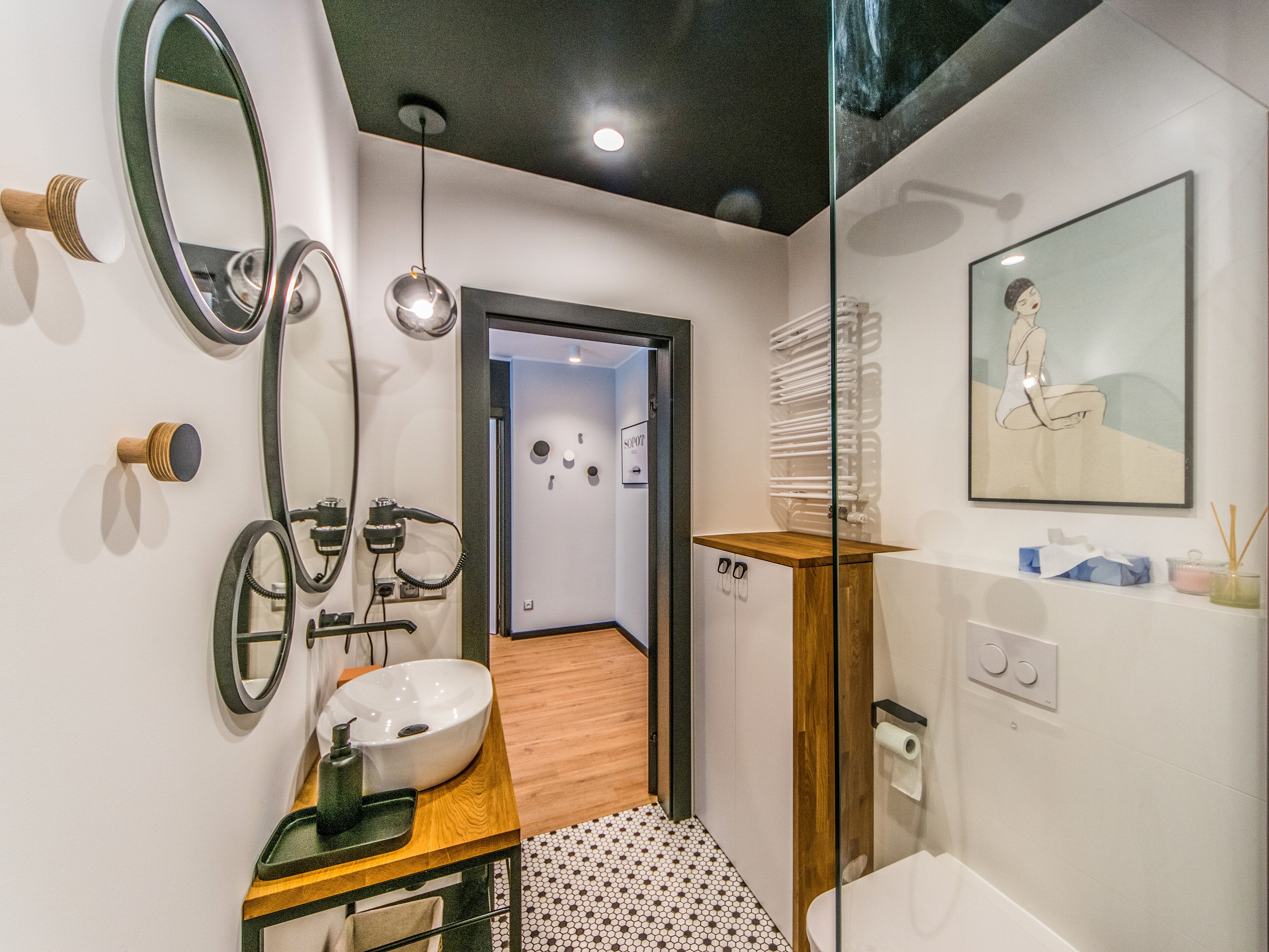 A modern bathroom with a wooden vanity, a large mirror, and a sink. There is a shower area with a glass door and a toilet with a paper towel holder.
