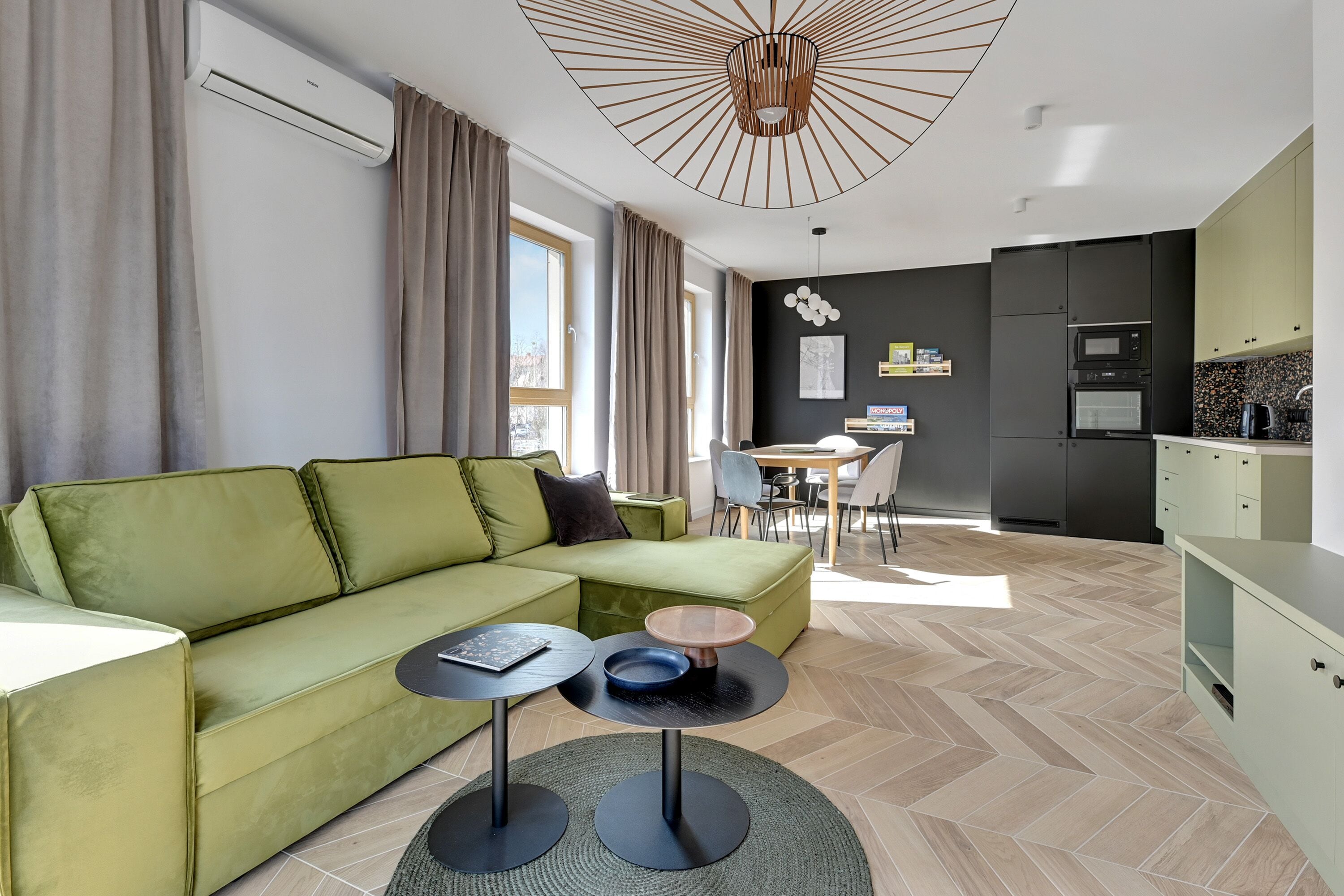 Ein modernes Wohnzimmer mit einem grünen Sofa, einem kleinen runden Tisch und einer Küchenzeile mit Esstisch und Stühlen.