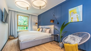 A modern bedroom with a large bed, a chair, a potted plant, and artwork on the wall.