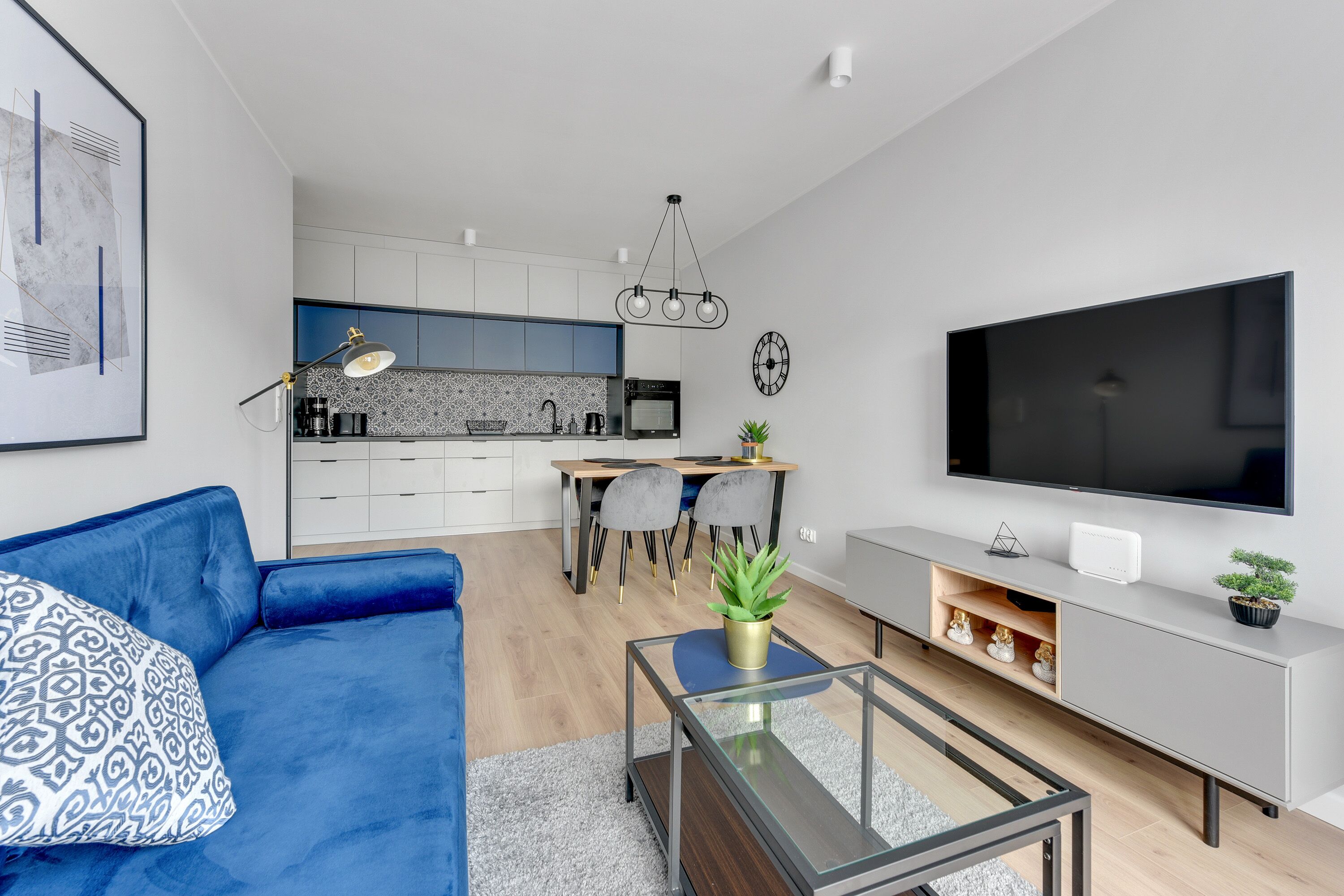 A modern living room with a blue sofa, a glass coffee table, and a grey entertainment unit with a flat-screen TV.