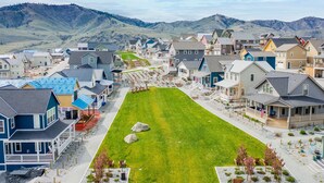 Zona residencial con casas, una plaza central con césped y montañas al fondo.