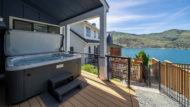 Un jacuzzi en una terraza de madera con vista a un lago y colinas.