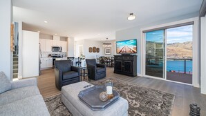Una sala de estar moderna con un sofá gris, una mesa de centro con objetos decorativos, un televisor de pantalla plana y vistas al mar a través de amplias puertas correderas.