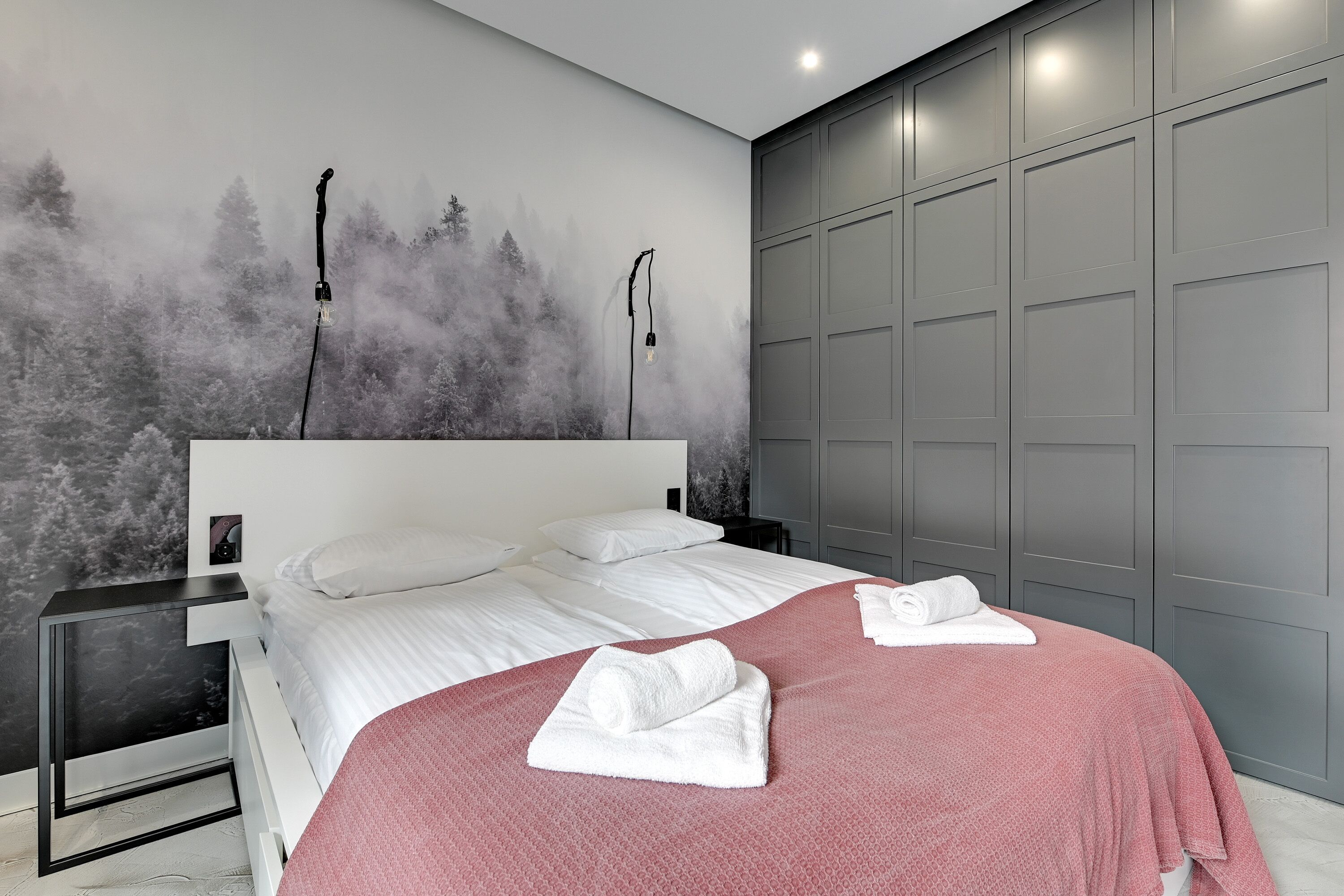 Ein modernes Schlafzimmer mit einem großen Bett, einem grauen Kleiderschrank und einer Wandmalerei eines Waldes.