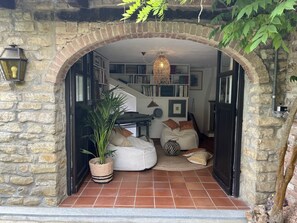 Un rincón acogedor para leer con un arco de piedra, un sillón de peluche blanco, una planta en maceta y una lámpara colgante.