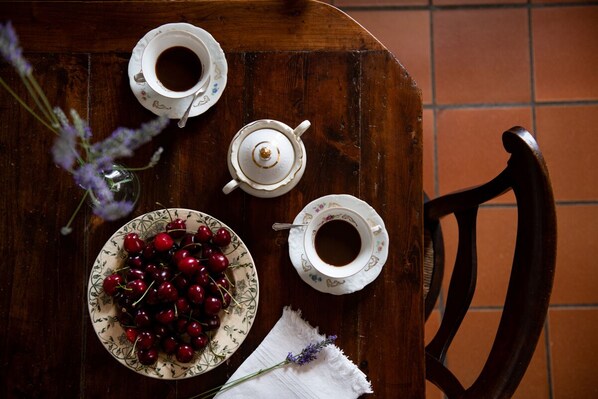 Una mesa de madera con dos tazas blancas, un hervidor, un plato de cerezas y un jarrón con lavanda.