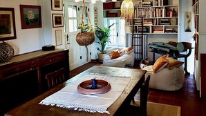 Un coin repas chaleureux et bien éclairé, avec une table en bois, des lampes suspendues et une bibliothèque remplie de livres.