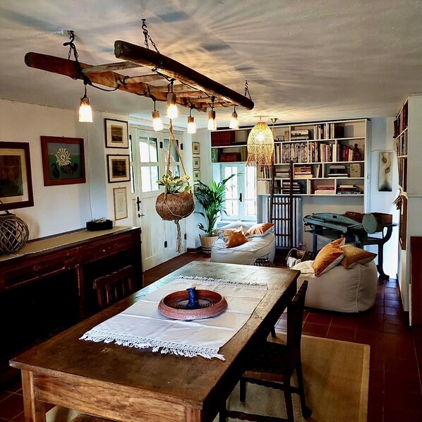Un comedor acogedor y bien iluminado, con una mesa de madera, luces colgantes y una estantería llena de libros.