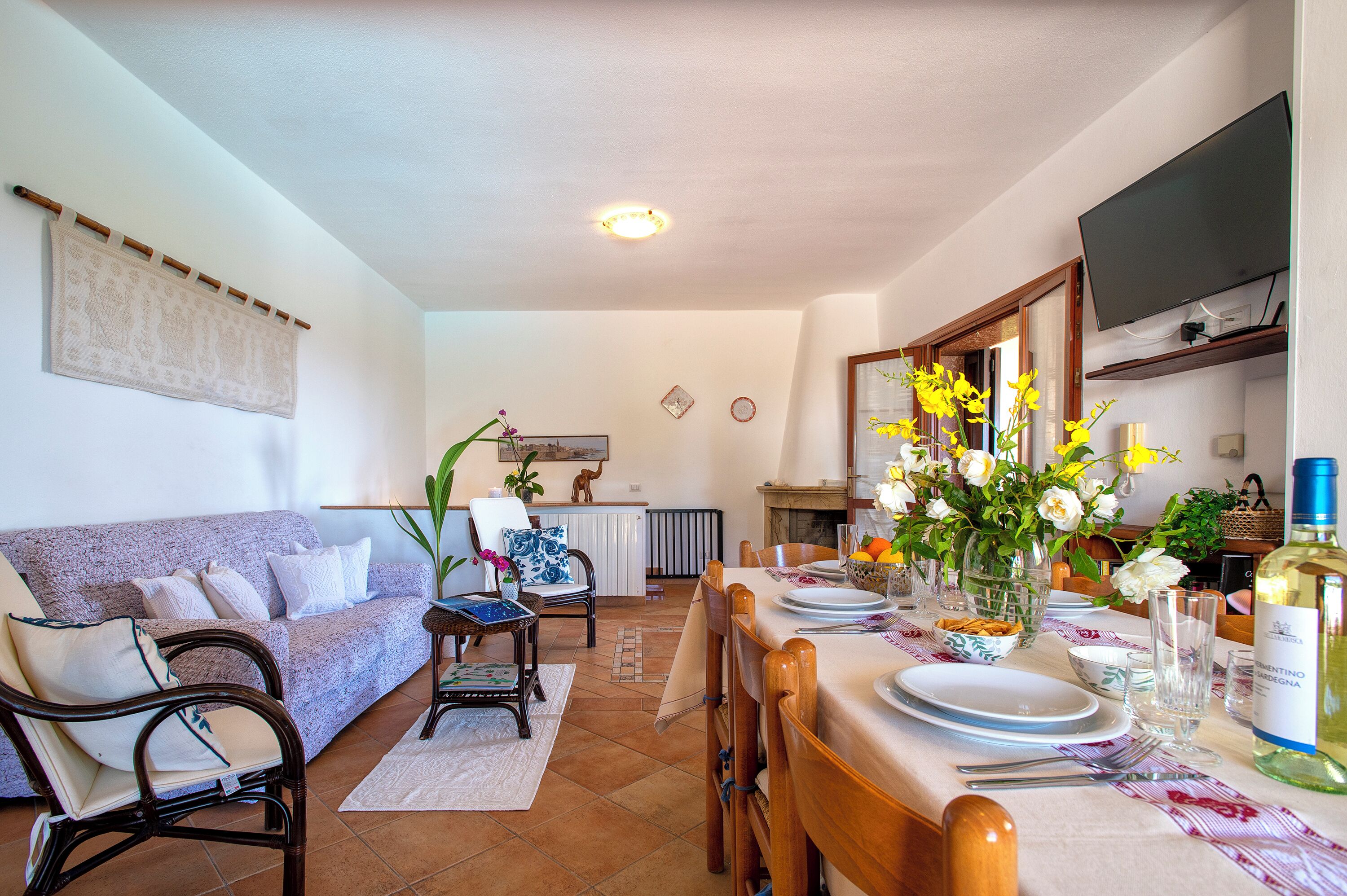 A dining area with a table set for four, a sofa, and a kitchen in the background.