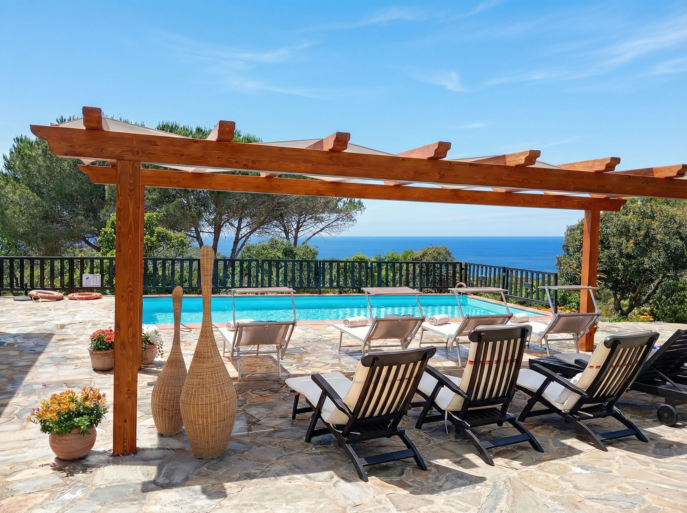 A poolside area with a pergola, lounge chairs, and a view of the sea.