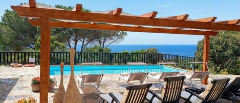A poolside area with a pergola, lounge chairs, and a view of the sea.