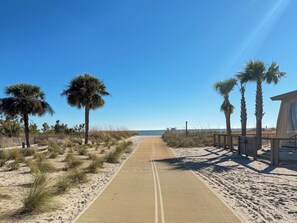 A sandy beach path with palm trees and a wooden structure on the right.