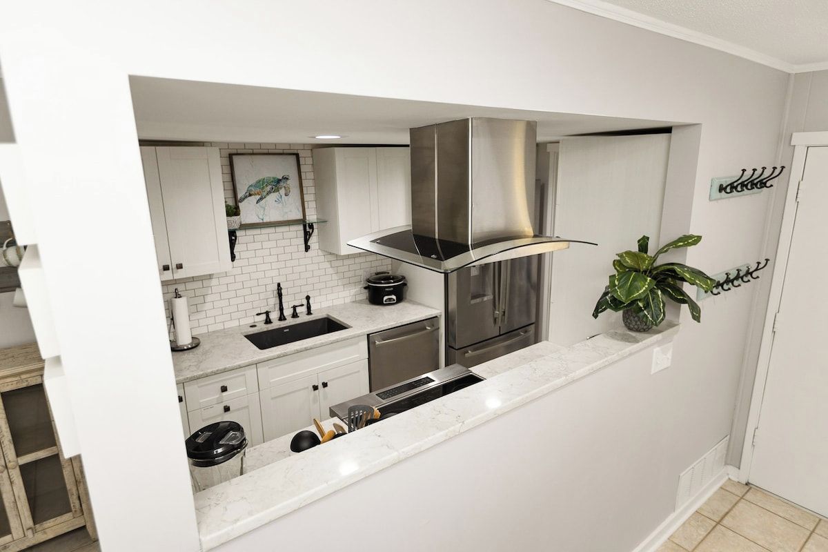 Cozinha moderna com armários brancos, eletrodomésticos de aço inoxidável e uma ilha central com forno embutido.