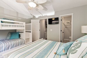 Ein Zimmer mit Etagenbetten, einem Deckenventilator, einem Fernseher und einer Tür zu einem Badezimmer.