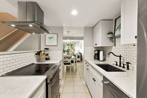 A modern kitchen with white cabinetry, a stainless steel range hood, and a central island with a sink.