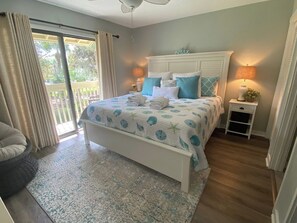 Un dormitorio con cama, mesita de noche, lámpara y vista al exterior.