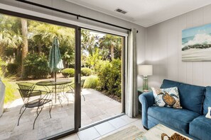 Una habitación con una puerta corrediza de vidrio que da a un patio con mobiliario exterior y vistas a zonas verdes.