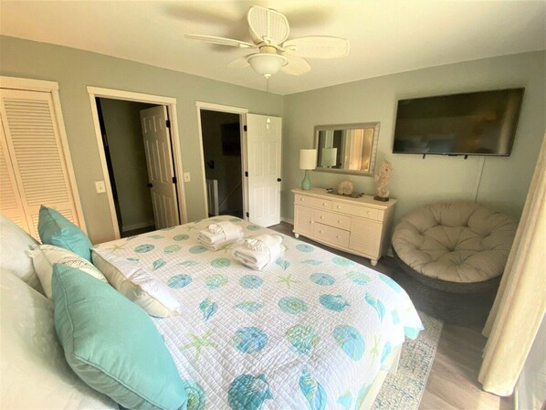 Un dormitorio con cama, cómoda, silla, ventilador de techo y televisor.