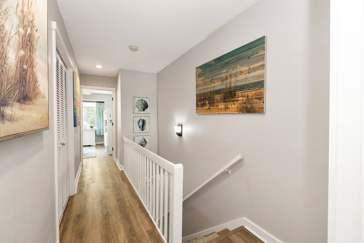 A hallway with a wooden floor, white railing, and artwork on the walls.