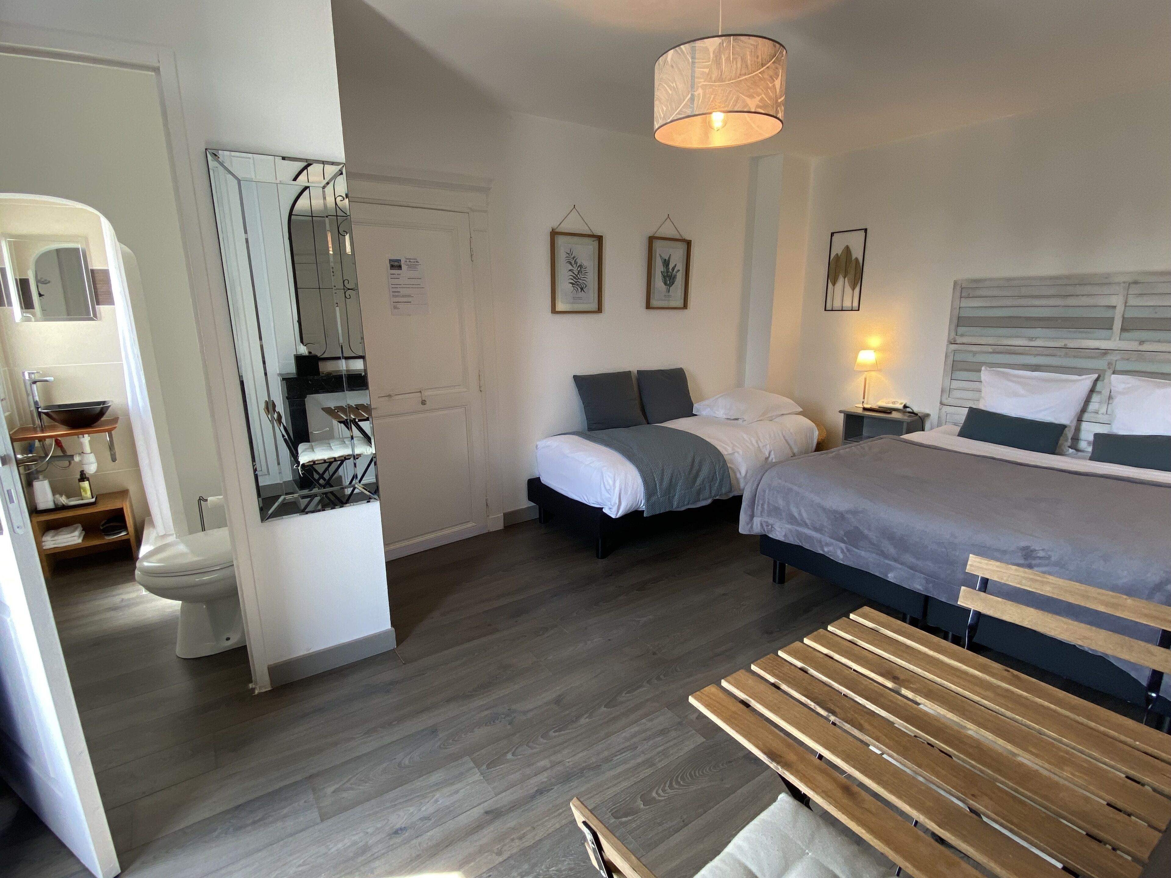 A bedroom with two beds, a bedside table, a hanging light fixture, a mirror, and a wooden bench.