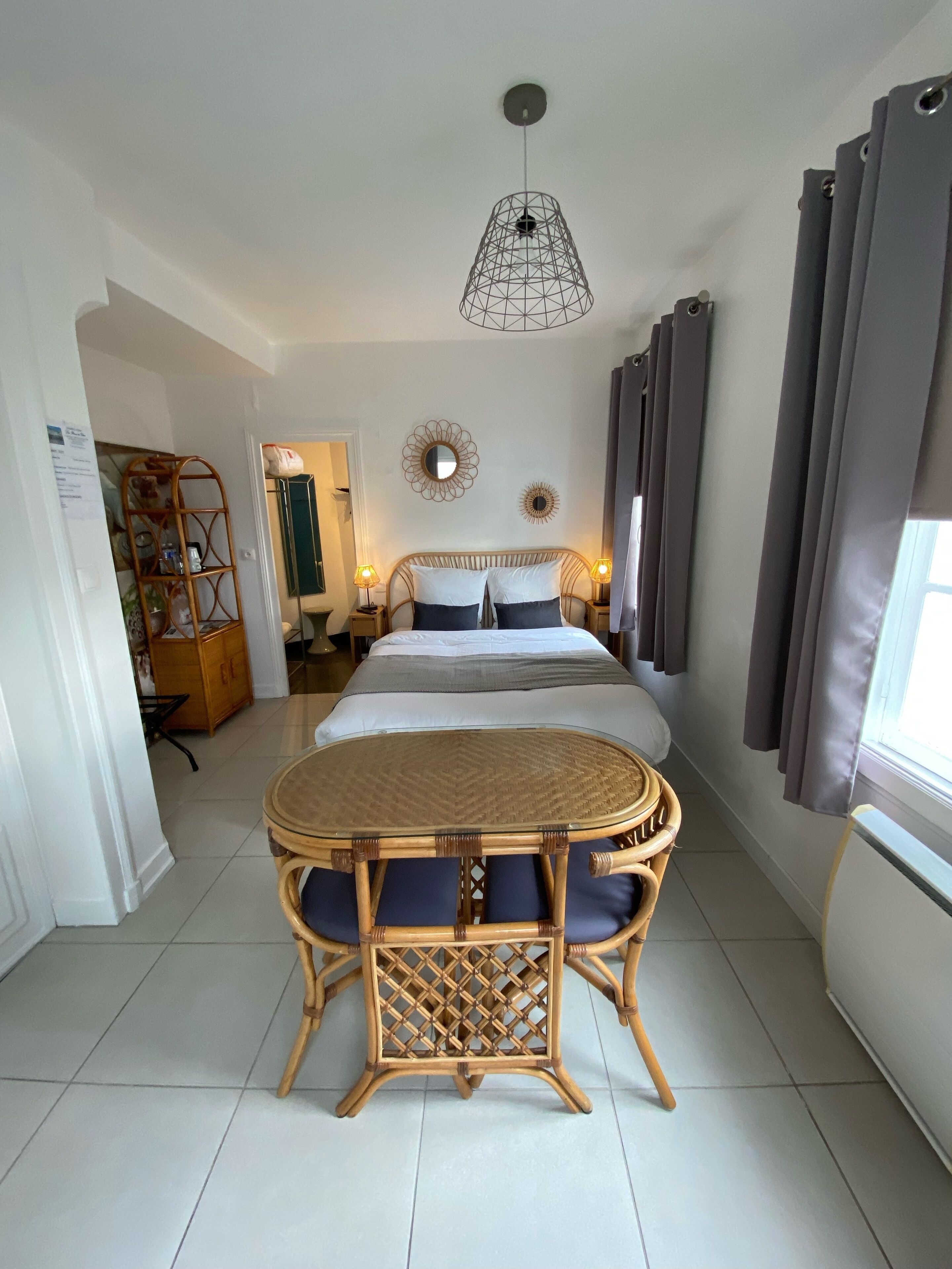 Ein Schlafzimmer mit einem Bett, Nachttischen, einer Hängelampe, einem Zier-Spiegel und einem Fenster mit Vorhängen.