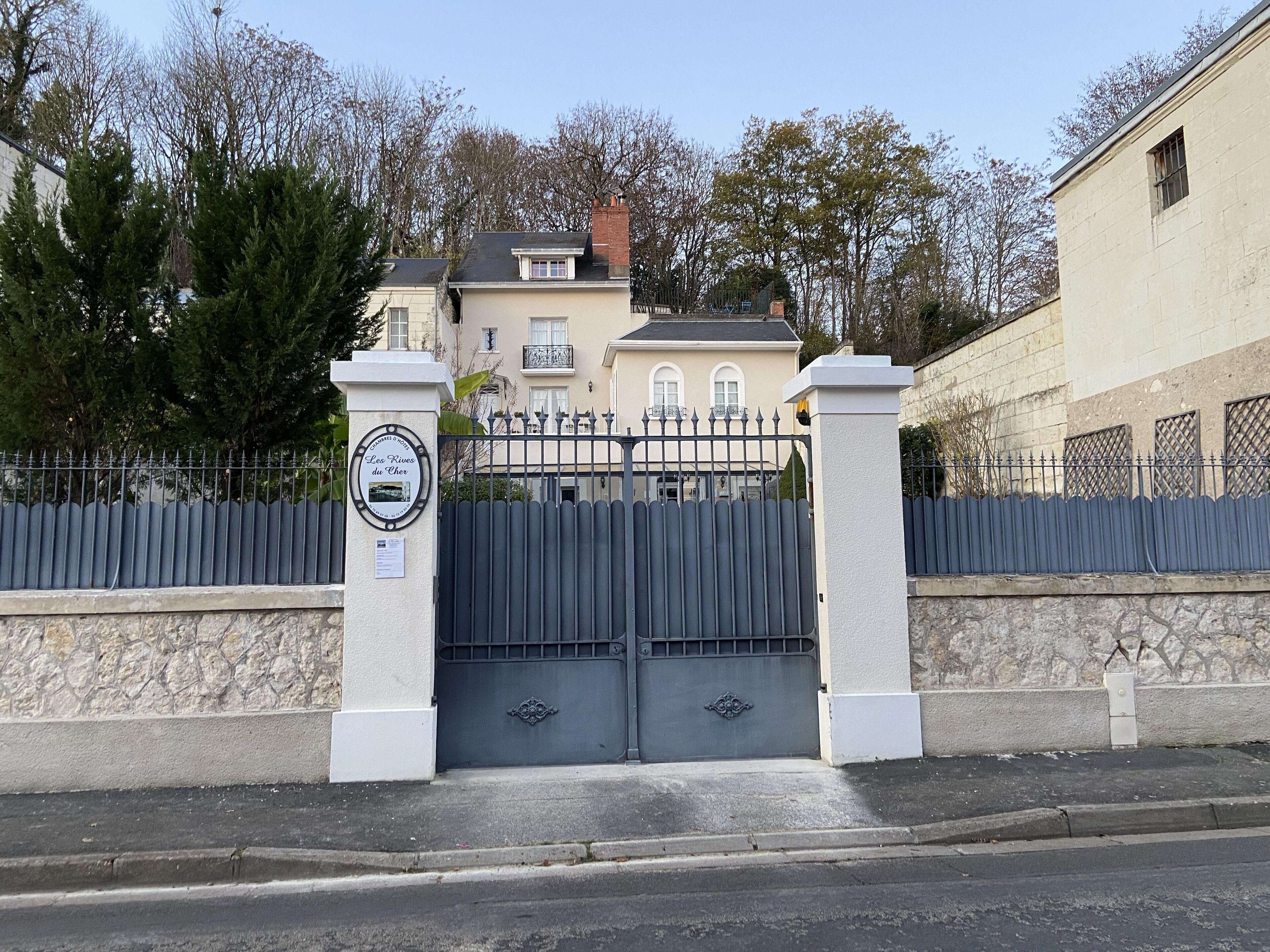 Una entrada con reja a una propiedad residencial, con muro de piedra y portón metálico.