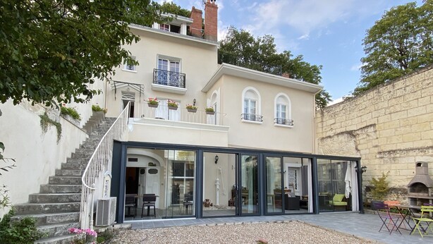 A two-story house with a glass-enclosed patio, a stone wall, and a staircase leading to the upper floor. - Les Rives du Cher (Montrichard Val de Cher)