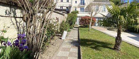A pathway leading to a building with a stone facade, surrounded by greenery and a clear blue sky.