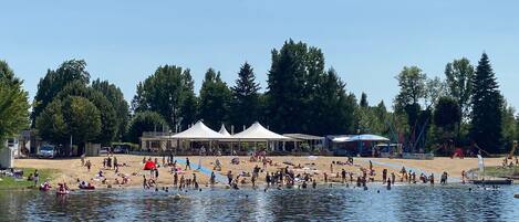 Un parque junto al lago con tiendas de campaña, una playa de arena y un parque infantil.