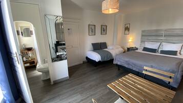 Een slaapkamer met twee bedden, een houten bankje, een plafondlamp en een badkamer met spiegel en wastafel.