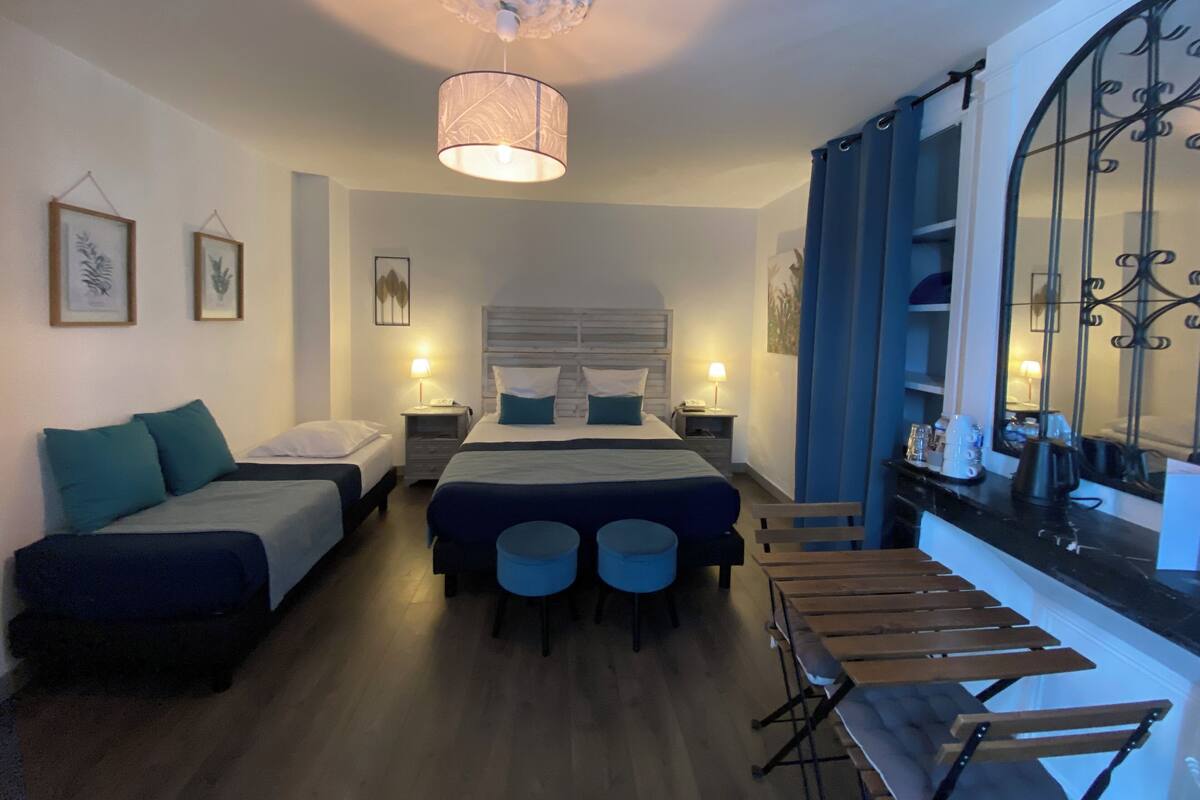 A hotel room with a large bed, two smaller beds, a dining table, and a window with curtains.