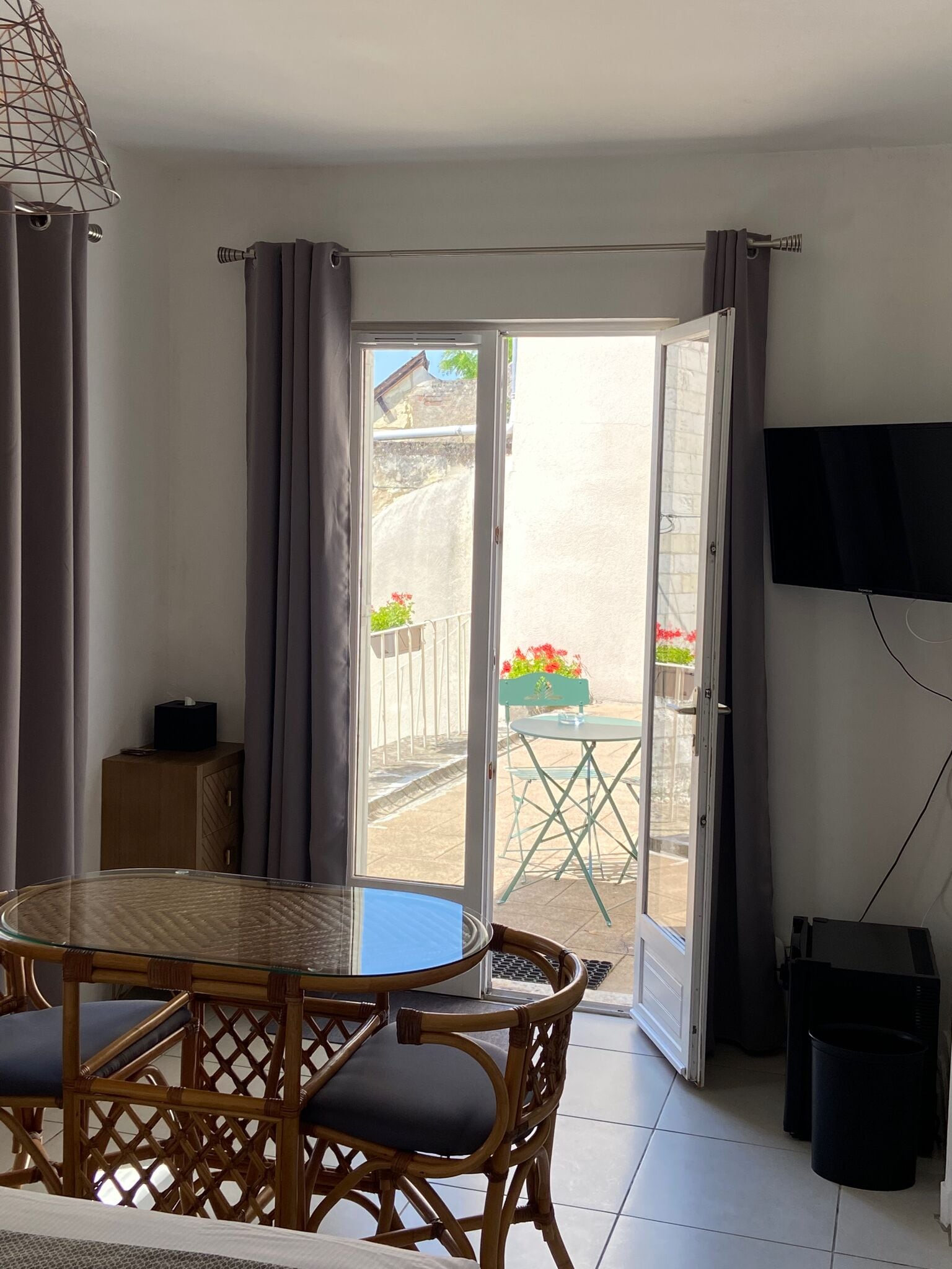 A room with a glass door leading to an outdoor area, a round table with chairs, a small cabinet, and a TV mounted on the wall.
