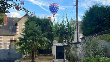 Een tuinpad dat leidt naar een gebouw, omgeven door weelderige begroeiing en een luchtballon aan de hemel.
