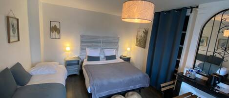 Una habitación de hotel con cama, dos mesitas de noche, un escritorio con silla y un espejo grande.