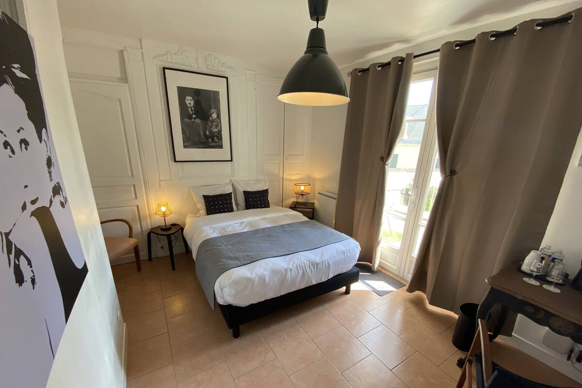 A bedroom with a bed, bedside lamps, a framed picture on the wall, and a view through the window.