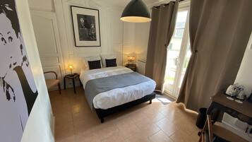 Une chambre à coucher avec un lit, des lampes de chevet, un tableau encadré au mur et une vue par la fenêtre.