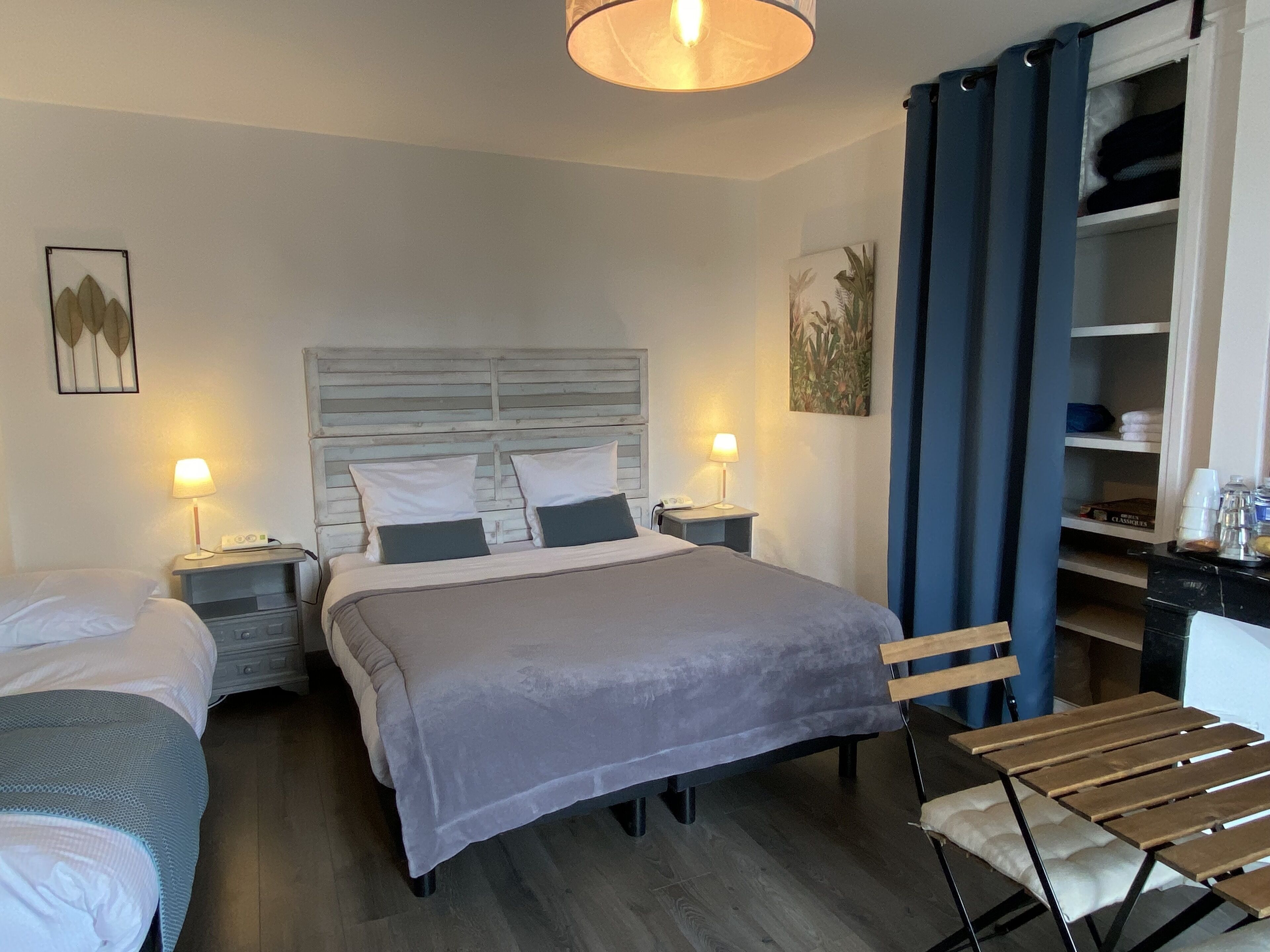 A hotel room with a bed, two bedside tables with lamps, a desk with a chair, and a wardrobe.