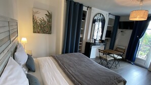 A bedroom with a bed, a nightstand, a lamp, a painting, a desk with a chair, a window with curtains, and a balcony. - Les Rives du Cher (Montrichard Val de Cher)