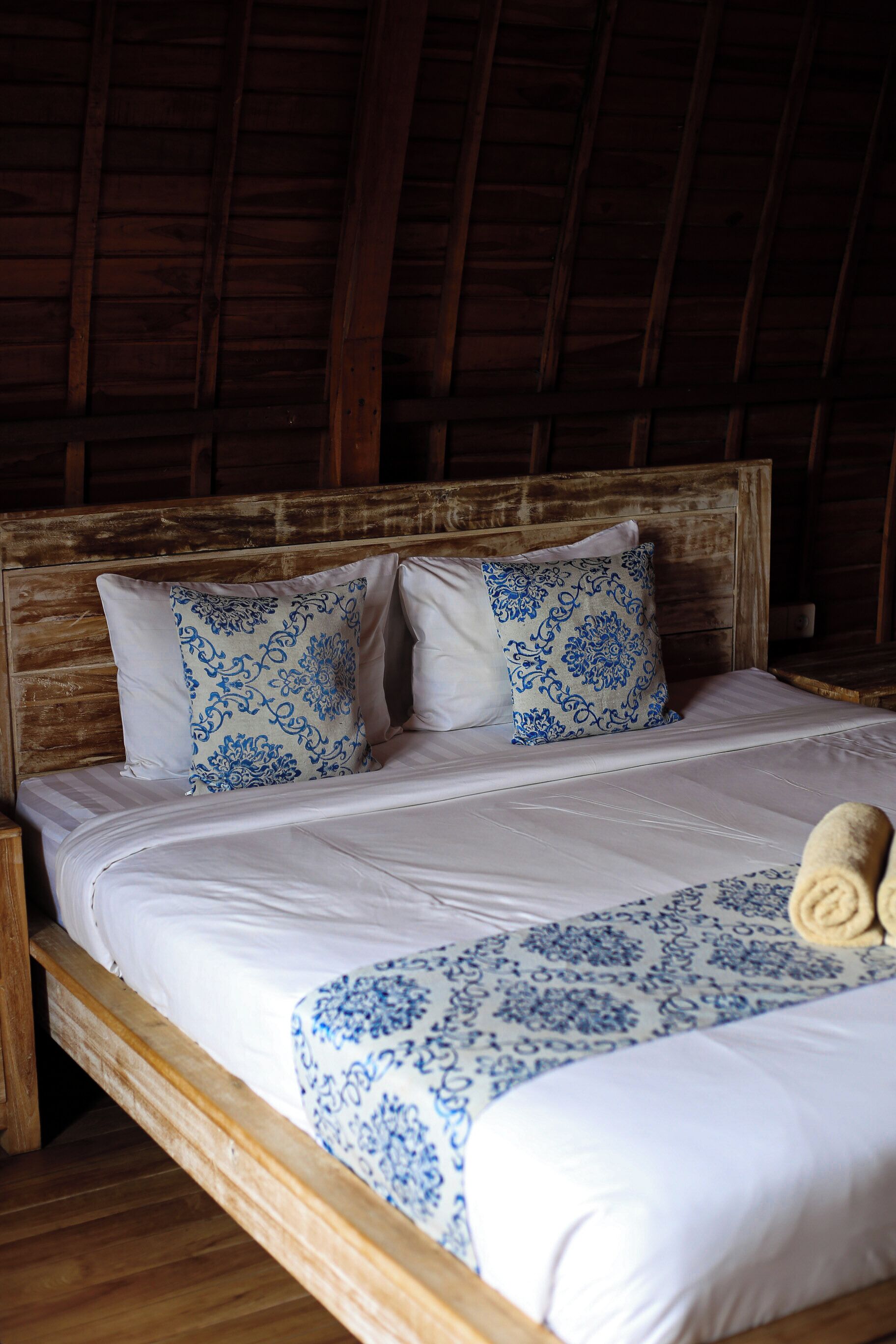 A wooden-framed bed with white bedding and blue patterned pillows.