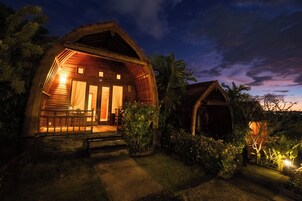 A wooden cabin with a porch, surrounded by vegetation.