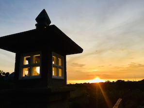 Ein kleines Steinhaus mit pyramidenförmigem Dach und zahlreichen Fenstern vor einem Sonnenuntergangshimmel.