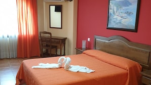 Een hotelkamer met een bed, een bureau, een stoel, een schilderij aan de muur en een raam met gordijnen.