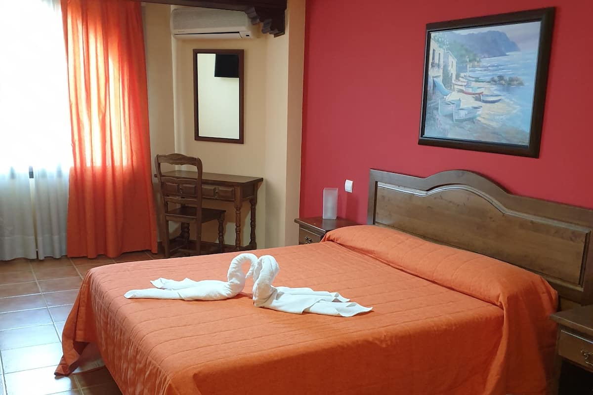 Een hotelkamer met een bed, een bureau, een stoel, een schilderij aan de muur en een raam met gordijnen.
