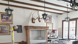Een bar met een zwart aanrecht, een open haard van baksteen, decoraties van gewei en rieten barstoelen.