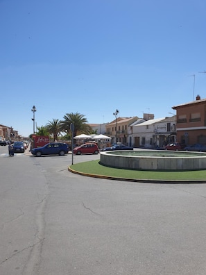Un carrefour giratoire avec une fontaine au centre, entouré de bâtiments et de voitures garées.