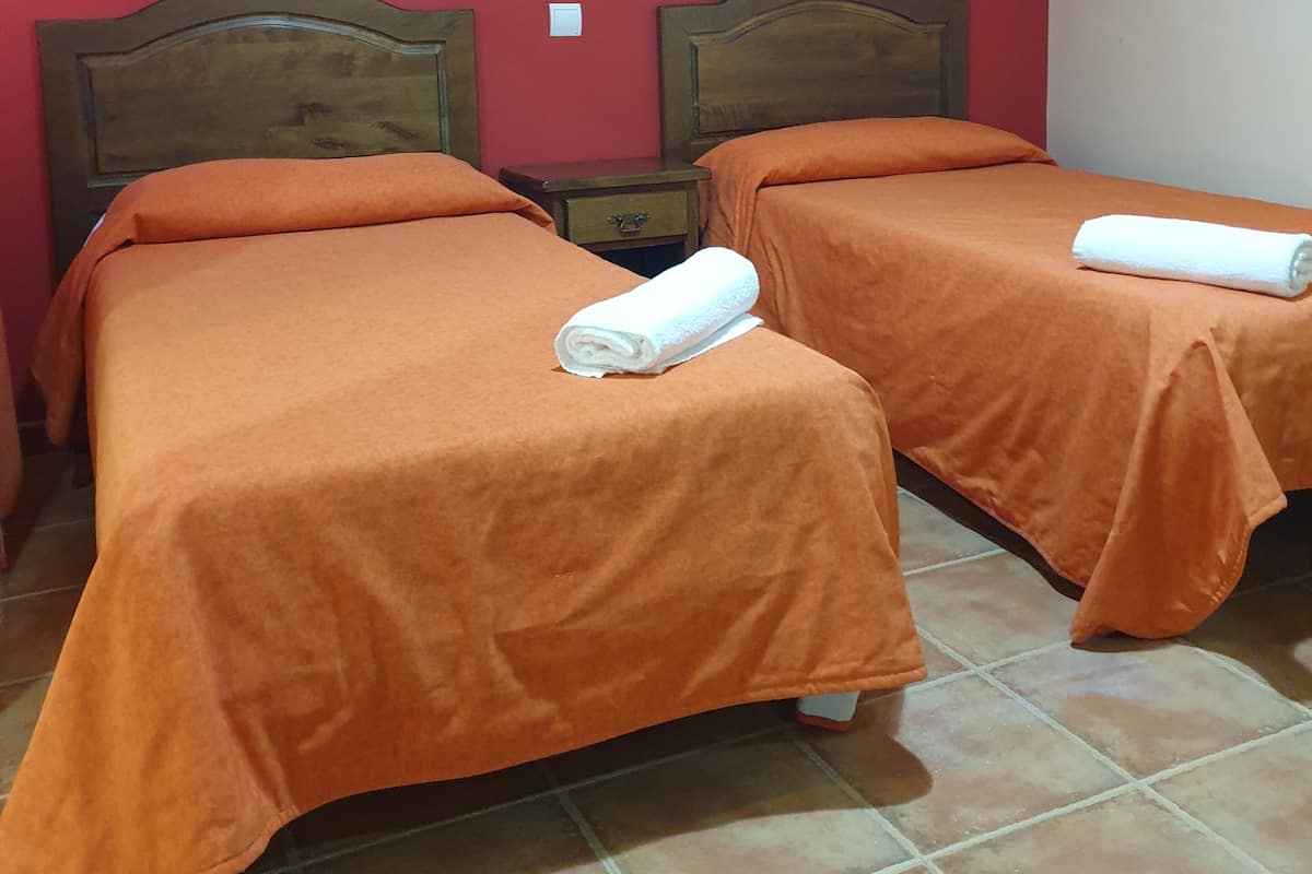 Een hotelkamer met twee bedden, oranje beddengoed, een houten hoofdbord, een airconditioner en een betegelde vloer.